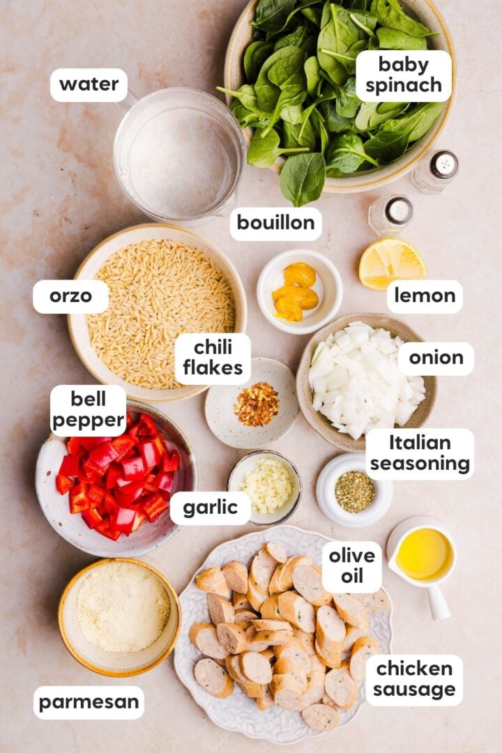 Ingredients for chicken sausage orzo skillet recipe displayed in small bowls on a beige counter