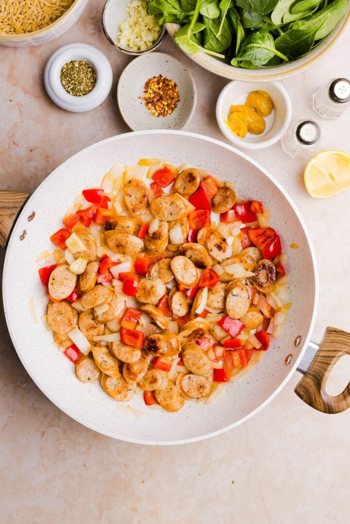 Peppers and onions added to chicken sausage in a large white pan