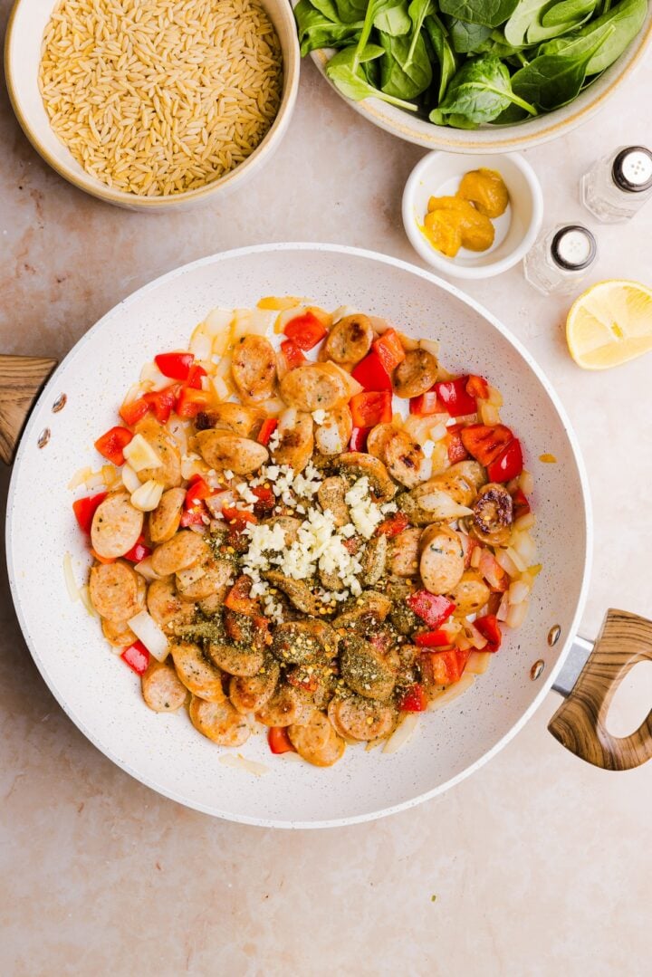 Garlic and seasonings added to a pan with cooked peppers, onions and chicken sausage