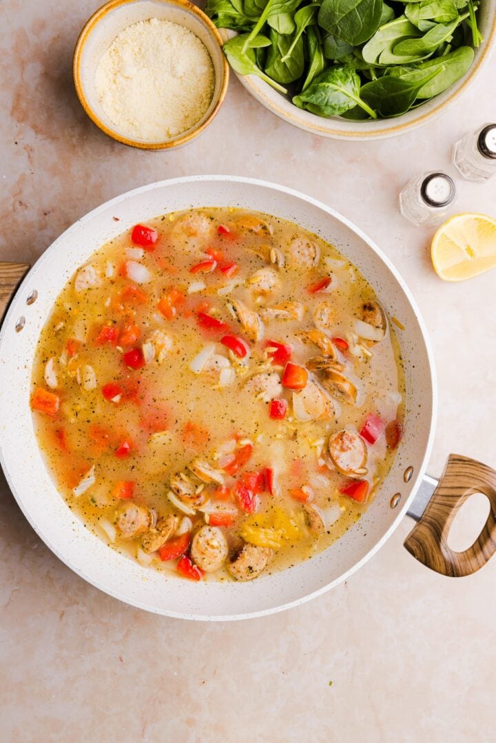 Broth added to a pan with other ingredients for chicken sausage orzo skillet