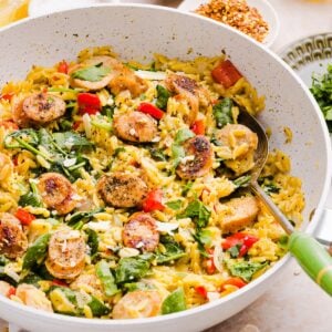 photo of chicken sausage orzo styles in a large white pan, with a silver serving spoon with a green handle