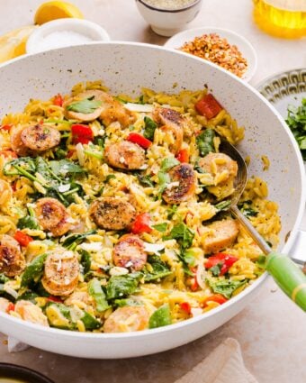 photo of chicken sausage orzo styles in a large white pan, with a silver serving spoon with a green handle