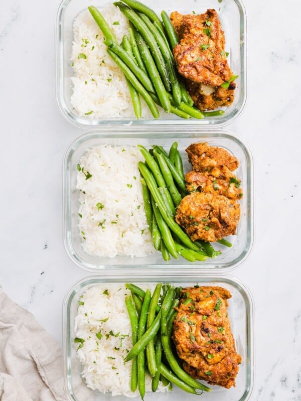 3 rectangular glass containers with rice, green beans, and meal prep chicken thighs