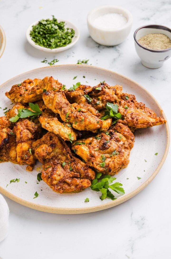 Meal prep chicken thighs on a white plate with fresh parsley