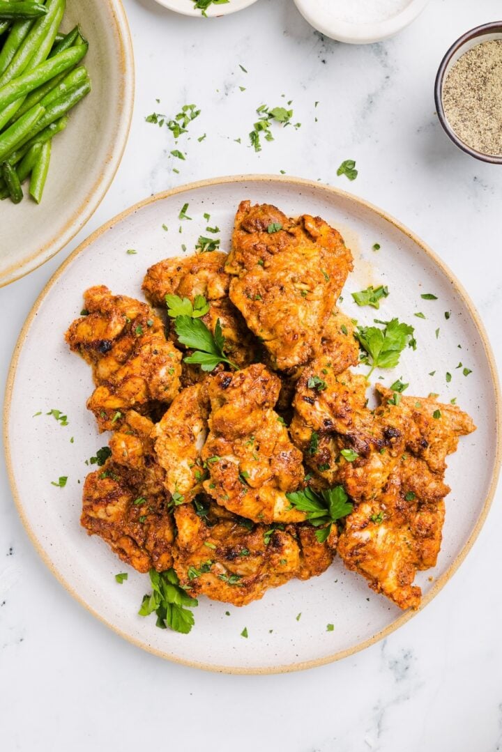 Overhead photo of meal prep chicken thighs on a white plate, garnished with parsley
