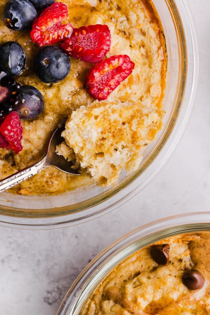 Close-up photo of a spoon taking a bite out of a protein pancake bowl, topped with berries and maple syrup.