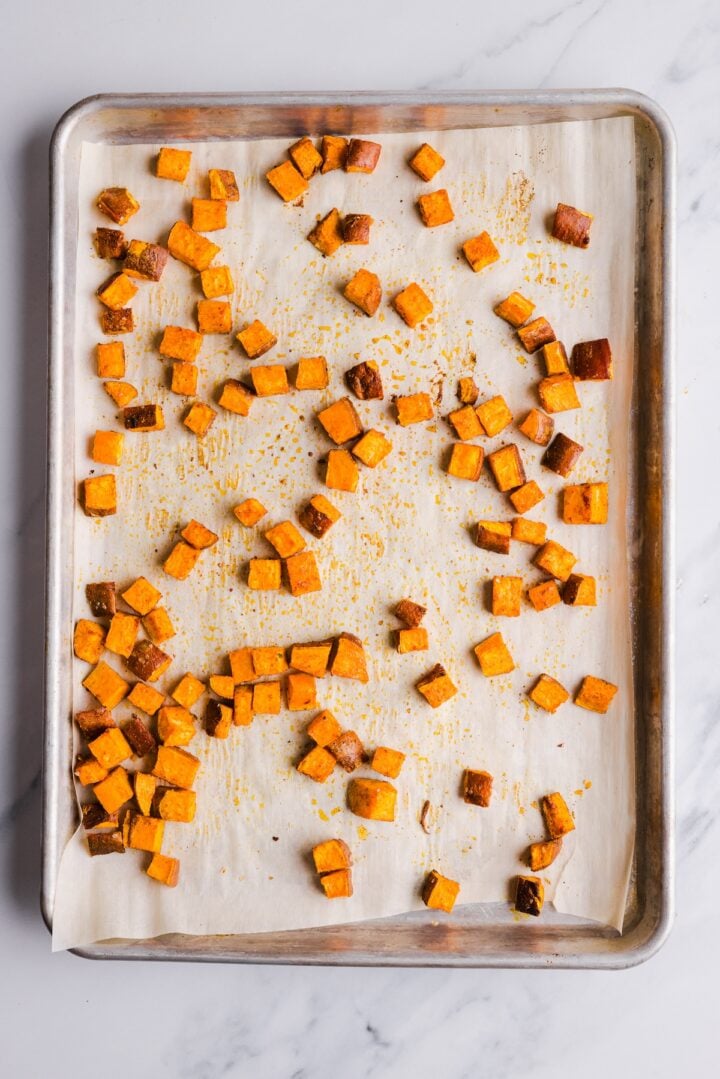 Cooked cubed and roasted sweet potatoes on a parchment-lined sheet pan