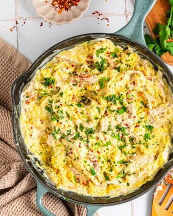 Chicken alfredo spaghetti squash in a pan, topped with red pepper flakes and parsley
