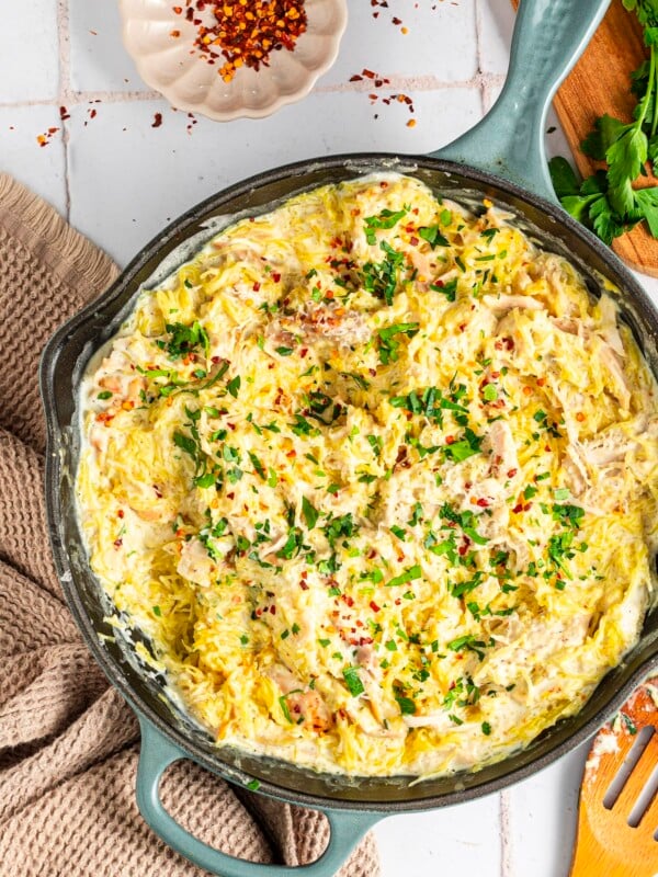 Chicken alfredo spaghetti squash in a pan, topped with red pepper flakes and parsley