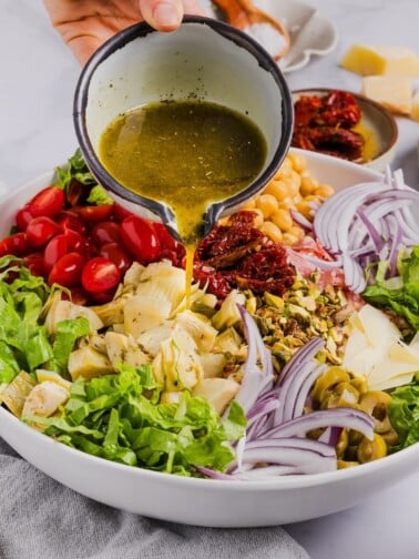 Dressing being poured over top of chopped antipasto salad