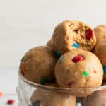 Close-up photo of cookie dough protein balls with mini m&m candies and mini chocolate chips, with a bite taken out of one
