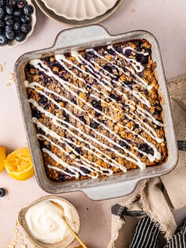 Lemon blueberry baked oatmeal in a baking dish, topped with a lemon yogurt drizzle