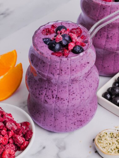 Close-up photo of two glasses with blueberry raspberry smoothie topped with frozen fruit