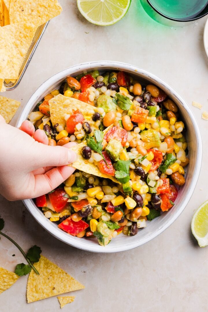 cowboy caviar couscous salad being scooped in a small bowl with a tortilla chip