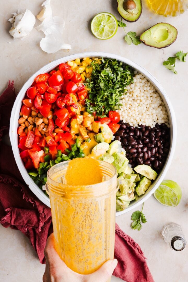 Dressing being poured over cowboy caviar couscous salad in a large bowl