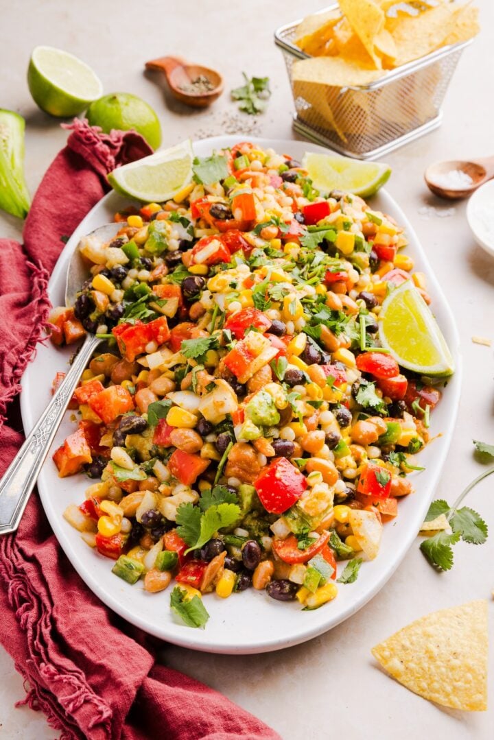 Cowboy caviar couscous salad prepared on a large serving platter, displayed with tortilla chips and lime wedges