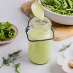 Green goddess ranch salad dressing in a glass jar near salad greens