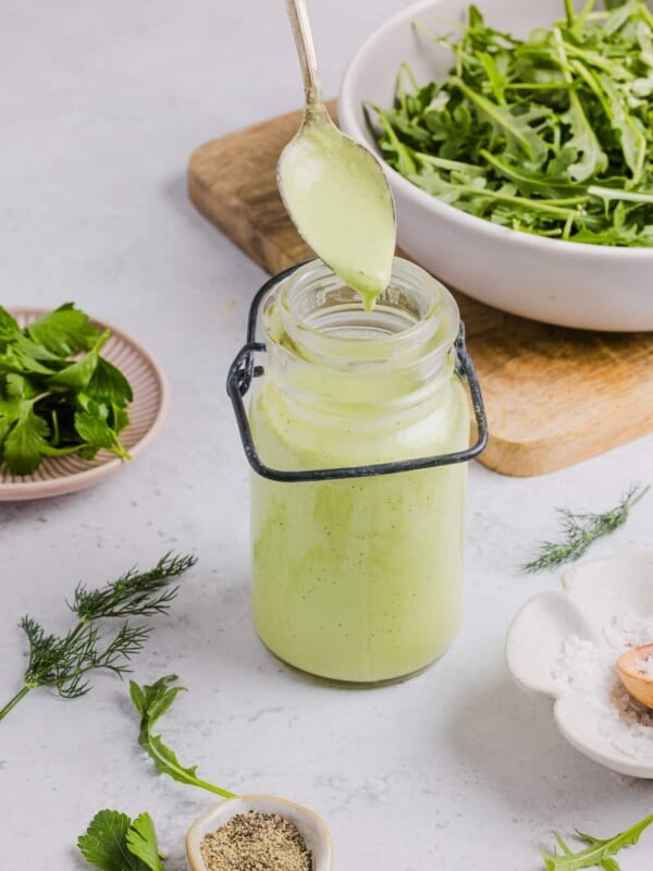 Green goddess ranch salad dressing in a glass jar near salad greens
