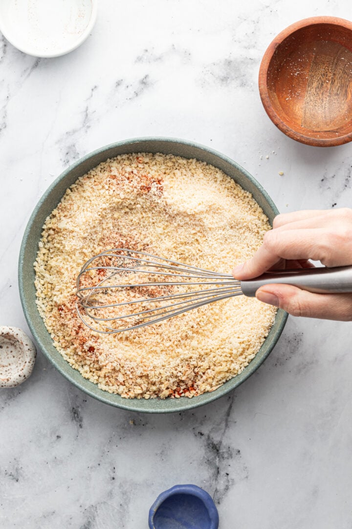 Breadcrumbs being mixed with seasoning in a large, shallow bowl.