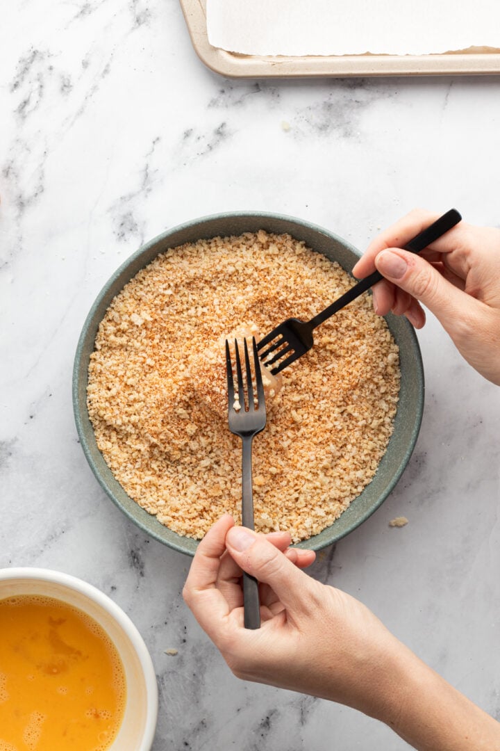 Forks coating chicken breast cube in breadcrumbs