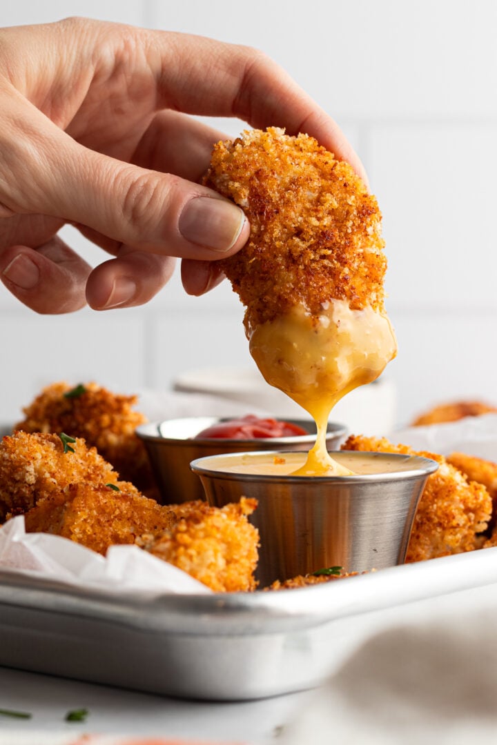 Woman's hand dipping chicken nugget into honey mustard