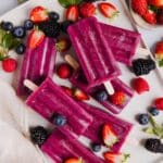 Fruit smoothie popsicles displayed on a white serving tray with fresh berries