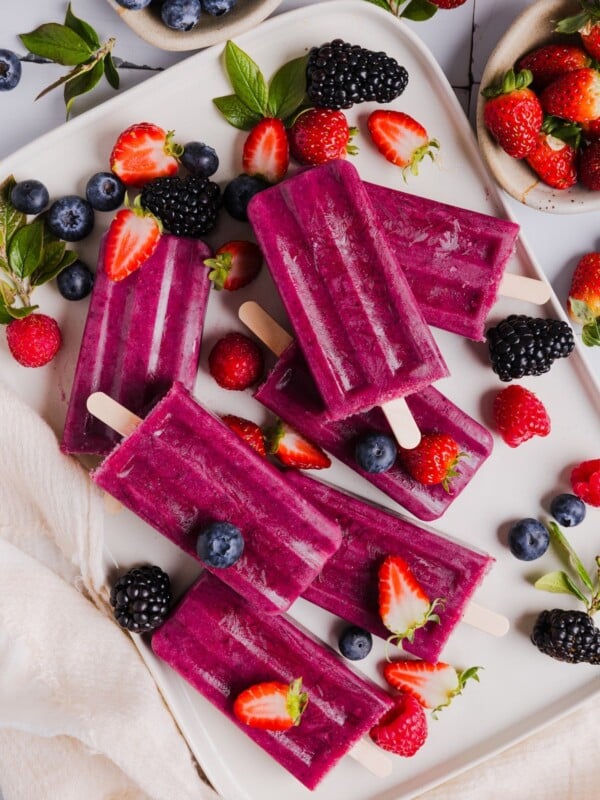 Fruit smoothie popsicles displayed on a white serving tray with fresh berries