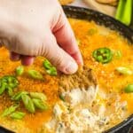 Woman's hand scooping protein jalapeno popper dip with a seedy cracker