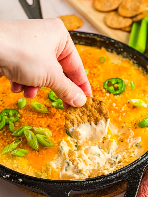 Woman's hand scooping protein jalapeno popper dip with a seedy cracker