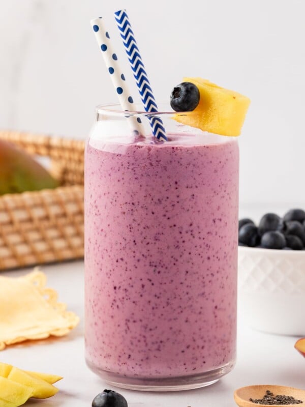 Single glass with mango blueberry smoothie, with two white and blue straws