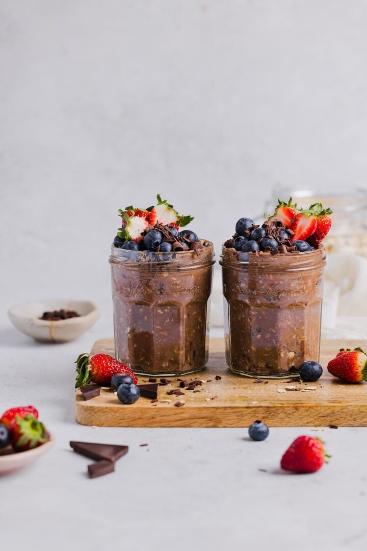 Two jars of chocolate protein overnight oats on a white marble counter, displayed on a wood serving board