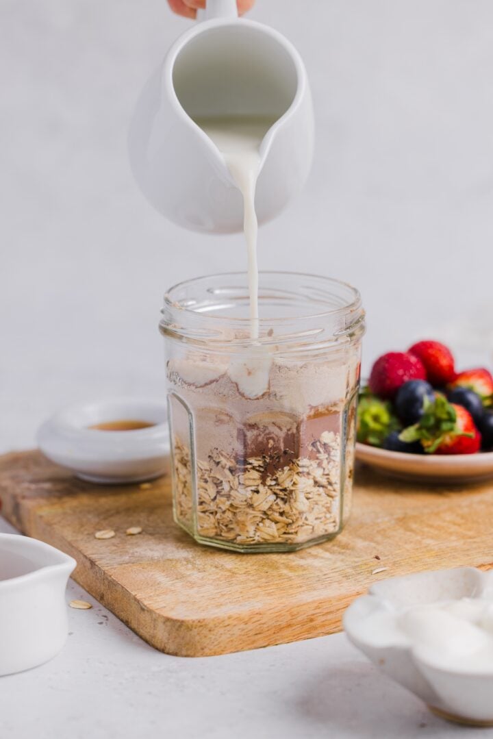 Milk being poured into container with chocolate overnight oats ingredients