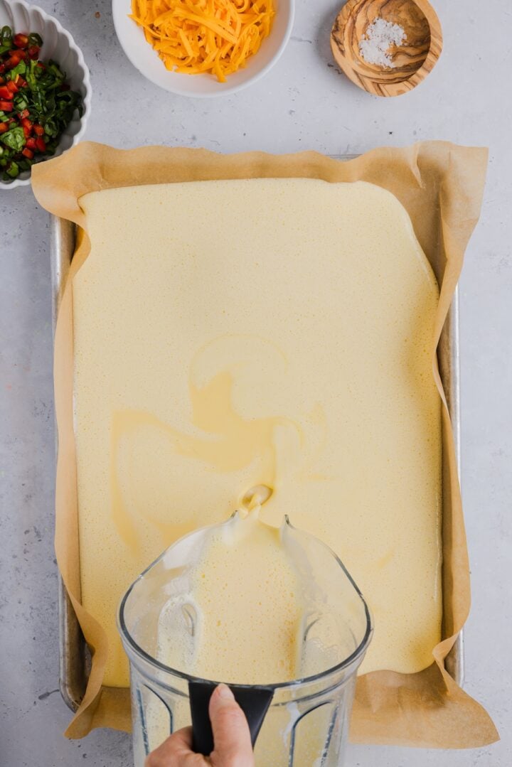 Blended eggs and cottage cheese being poured in a parchment-lined sheet pan.