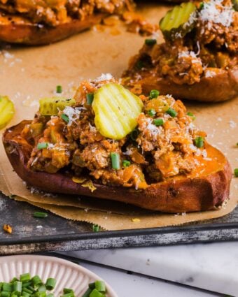 Stuffed sweet potato sloppy joes topped with grated cheese and pickle slices, on parchment paper
