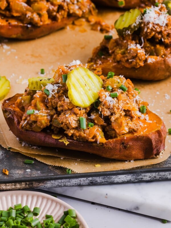 Stuffed sweet potato sloppy joes topped with grated cheese and pickle slices, on parchment paper