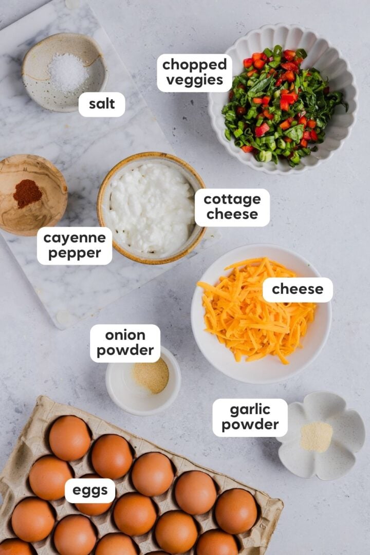 Labeled photo of ingredients for sheet pan eggs with cottage cheese, displayed in small bowls on a light grey marble counter