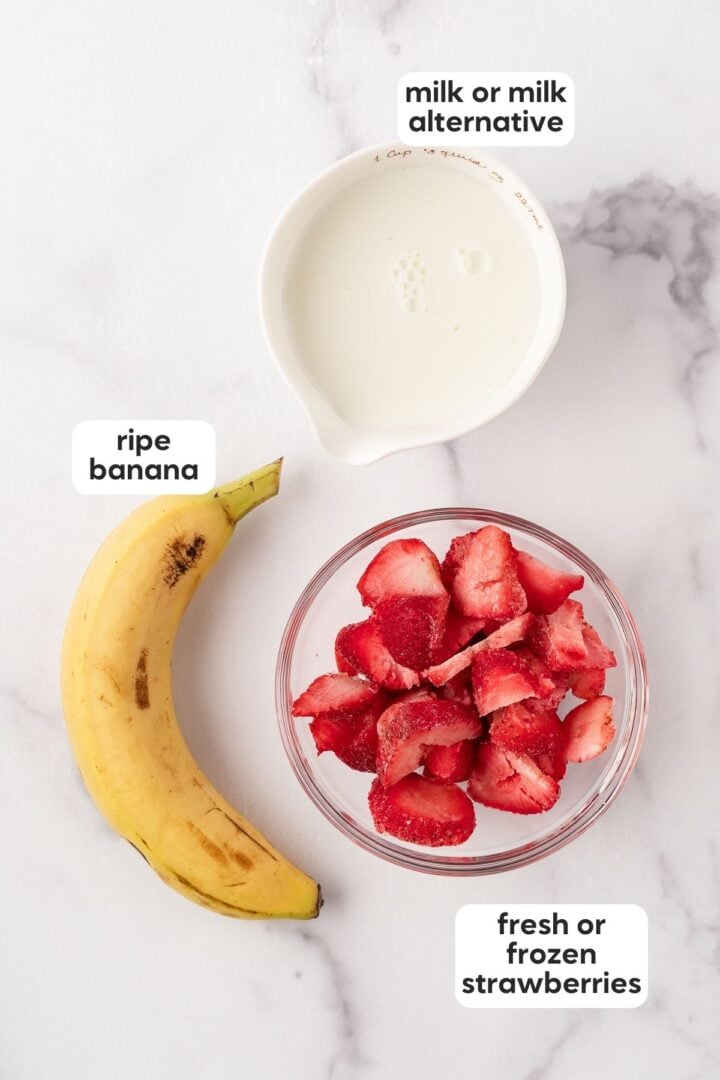 Labeled photo of 3-ingredient strawberry banana smoothie ingredients displayed in small bowls on a marble counter