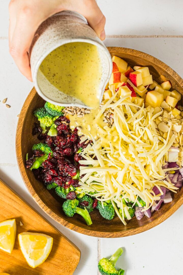 Broccoli Crunch Salad in a mixing bowl with honey lemon dressing being poured over it