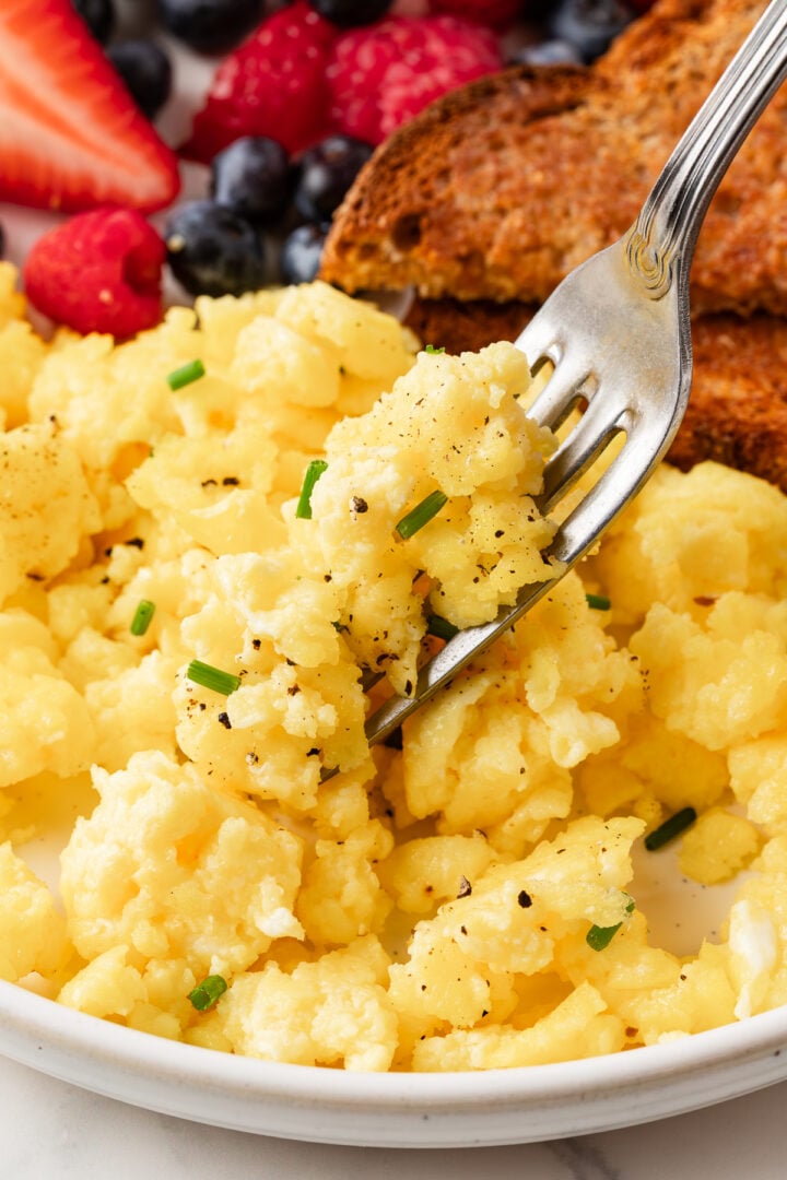 close-up photo of cottage cheese scrambled eggs on a fork, seasoned with diced chives