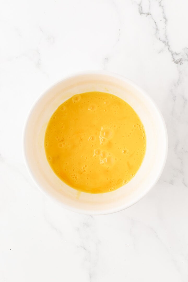 Eggs thoroughly whisked in a small white bowl.