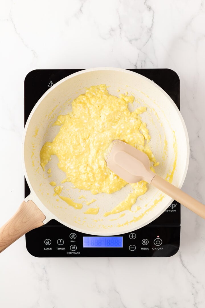 Cottage cheese eggs being scrambled in a non-stick pan over a hot plate.