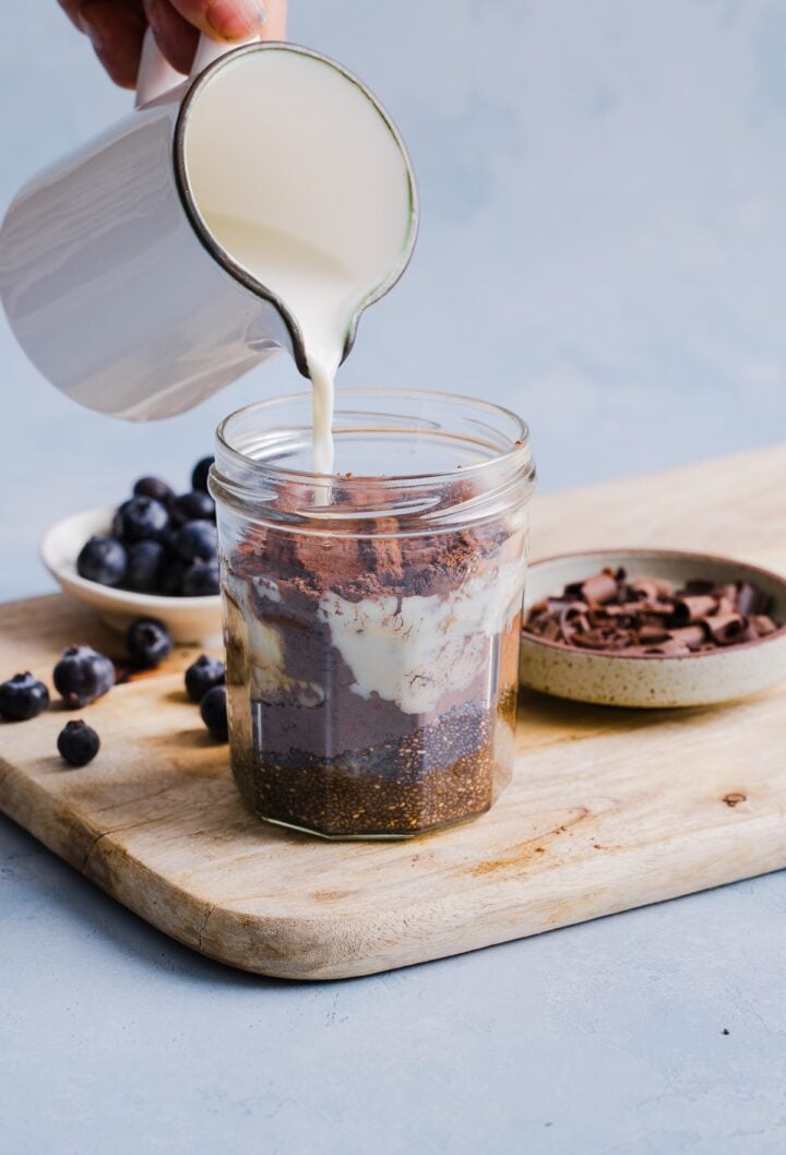 Milk being poured into a glass jar with other ingredients for chocolate chia pudding