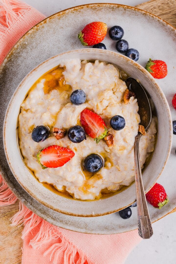 Overhead photo of egg white oatmeal in a bowl, with fresh berries and maple syrup