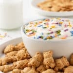 Protein dunkaroo dip in a small white bowl, surrounded by teddy graham cookies on a plate