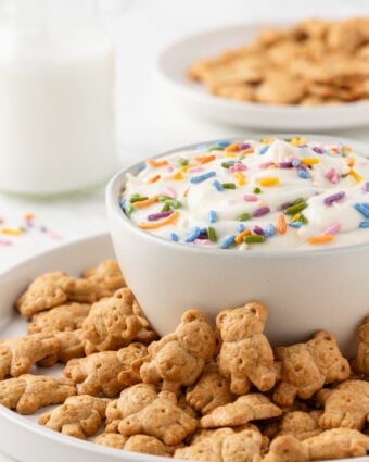 Protein dunkaroo dip in a small white bowl, surrounded by teddy graham cookies on a plate