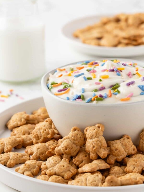 Protein dunkaroo dip in a small white bowl, surrounded by teddy graham cookies on a plate