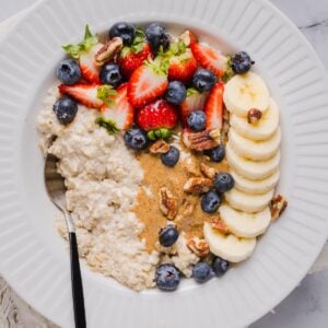 Protein oatmeal in a small white bowl, topped with berried, banana, and nut butter.