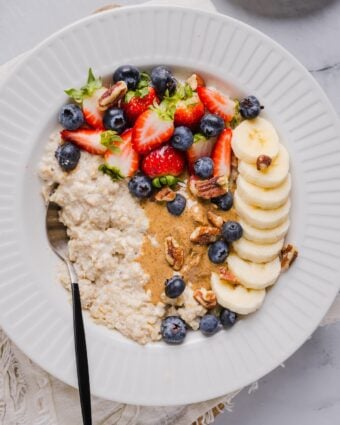 Protein oatmeal in a small white bowl, topped with berried, banana, and nut butter.