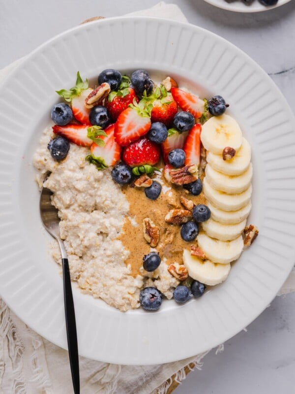 Protein oatmeal in a small white bowl, topped with berried, banana, and nut butter.