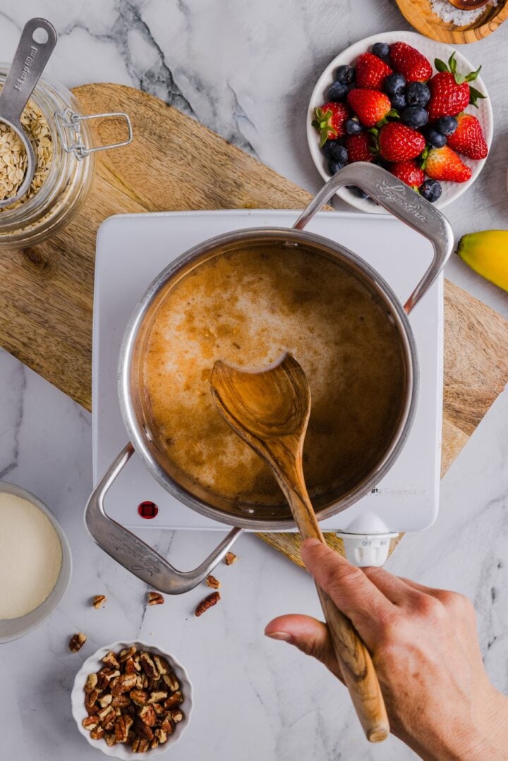 Ingredients for protein oatmeal in a pot, being stirred by a wooden spoon